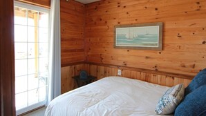A wooden-paneled room with a bed, a small table, and a window with curtains. - St. Martins Sea Caves · Oceanfront Retreat (Saint Martins Parish)