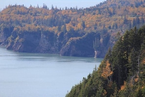 A coastal landscape with a body of water, forested hills, and a clear sky.