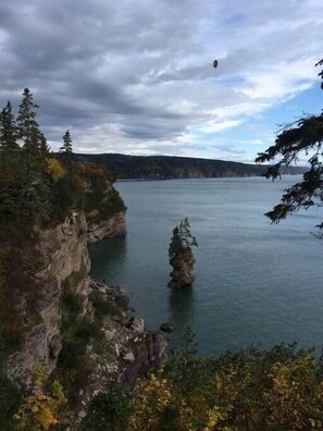 A coastal landscape with a rocky cliff, a small island, and a body of water under a cloudy sky.