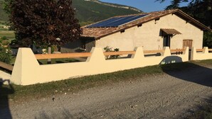 Un edificio rústico con techo inclinado y paneles solares, rodeado por un camino de grava y una valla de madera.