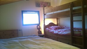 Quarto com uma cama beliche, uma cama de solteiro, uma janela e um radiador.