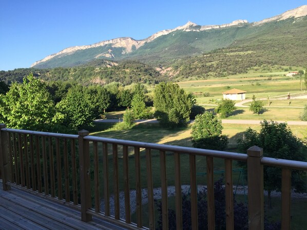A wooden deck with a view of a green landscape, including trees and a building in the distance. - Holiday house between lake and mountain (Serres)