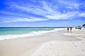Een strand met heldere lucht, rustige golven en enkele wandelaars.