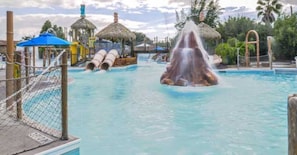 Un parc aquatique doté d’une fontaine centrale, de toboggans et de structures à toits de chaume.