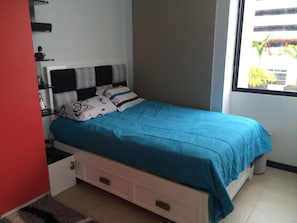 Una camera da letto con un letto, un comodino, una cassettiera e una finestra che si affaccia sul verde.