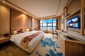 Ett hotellrum med en stor säng, ett skrivbord, en tv och utsikt över staden.