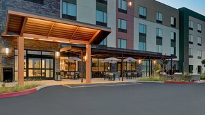 Entrada de hotel con área de estar al aire libre techada, fachada de piedra y un edificio de varios pisos con balcones.