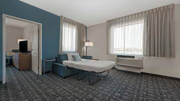 Una habitación de hotel con cama, escritorio, silla, lámpara y ventana con cortinas.