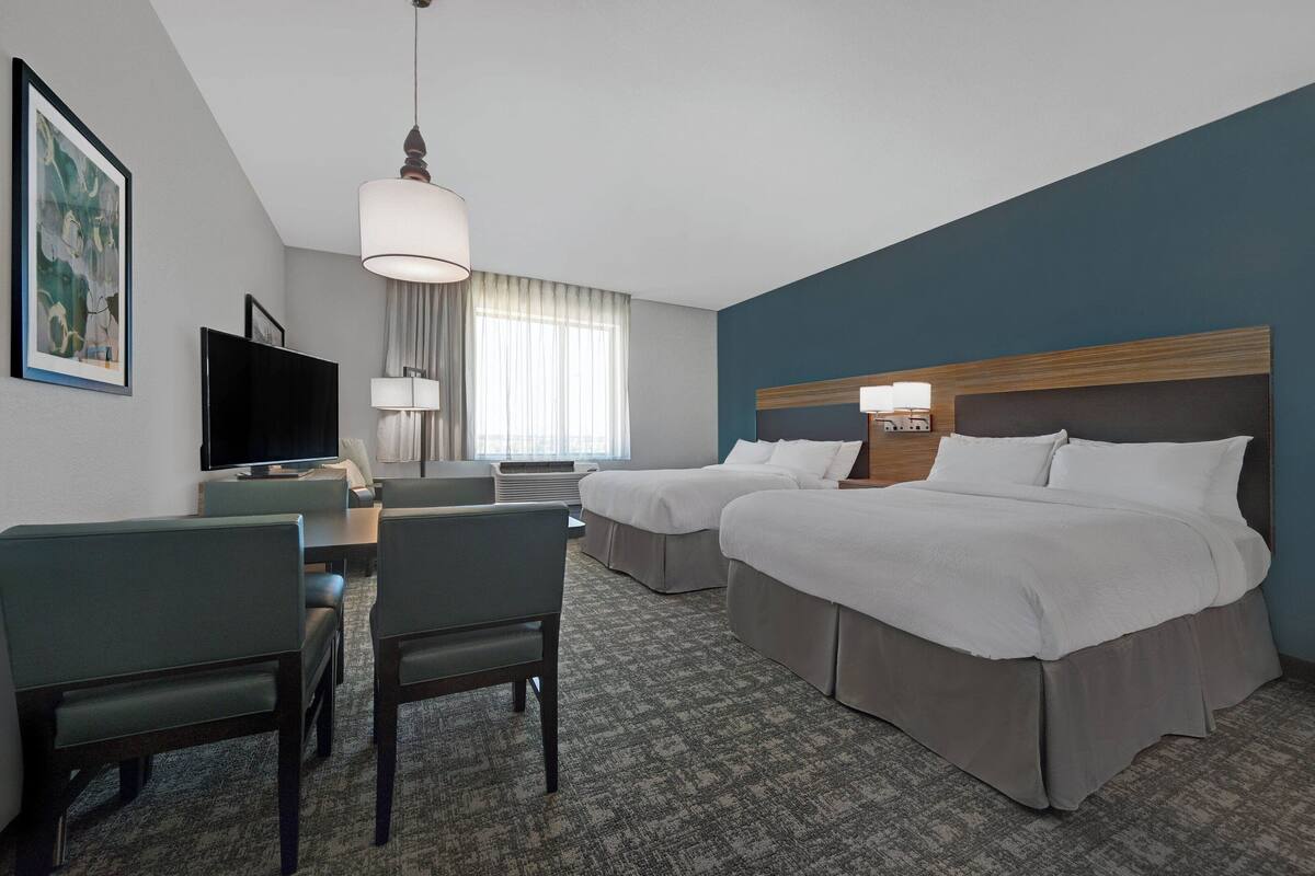A hotel room with two beds, a desk with a chair, a television, and a large window with curtains.