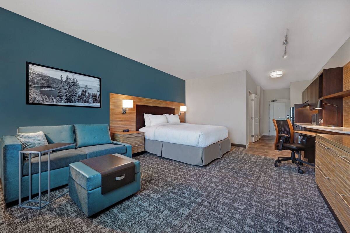 A modern hotel room with a bed, a sofa, a desk, and a chair.