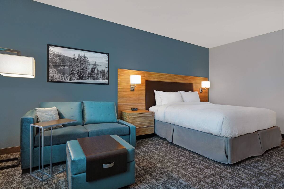 A hotel room with a bed, a sofa, a small table, and a nightstand.