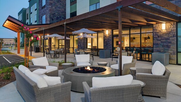Un patio exterior con mobiliario de mimbre, una chimenea y una zona de estar cubierta con sombrillas.