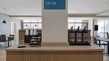 Uma estação de café moderna com um letreiro indicando “Na Conta da Casa” acima do balcão, uma máquina de café e diversos recipientes com café.