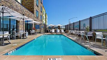 A swimming pool with a 5 FT 1.5 M depth marker, surrounded by lounge chairs and umbrellas, with a stone building in the background.