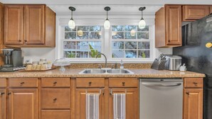 A kitchen with wooden cabinets, a stainless steel refrigerator, a sink, and hanging pendant lights.