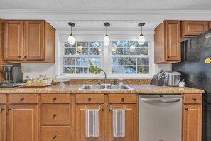 A kitchen with wooden cabinets, a stainless steel refrigerator, a sink, and hanging pendant lights.