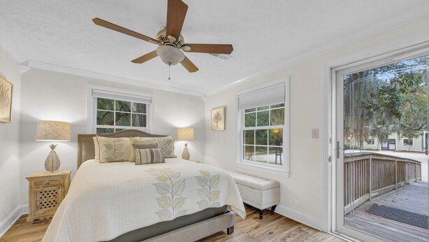 A bedroom with a bed, a ceiling fan, a nightstand, a bench, and a large window.
