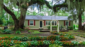 A house with a garden in front, surrounded by large trees.