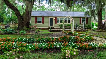A house with a garden in front, surrounded by large trees.