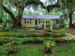 A house with a garden in front, surrounded by large trees.