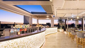 Een moderne bar met een gebogen toonbank, barstoelen en uitzicht over de stad.