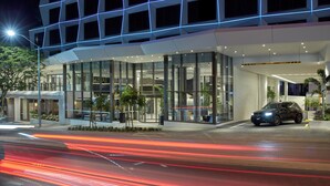 Een modern gebouw met een glazen gevel, een auto ervoor en een straat met lichtsporen.