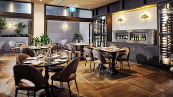 A restaurant with wooden flooring, multiple tables and chairs, a wine refrigerator, and potted plants.