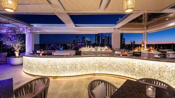 Zona de bar moderna con vista a la ciudad, un revoque de azulejos y diferentes disposiciones de asientos.