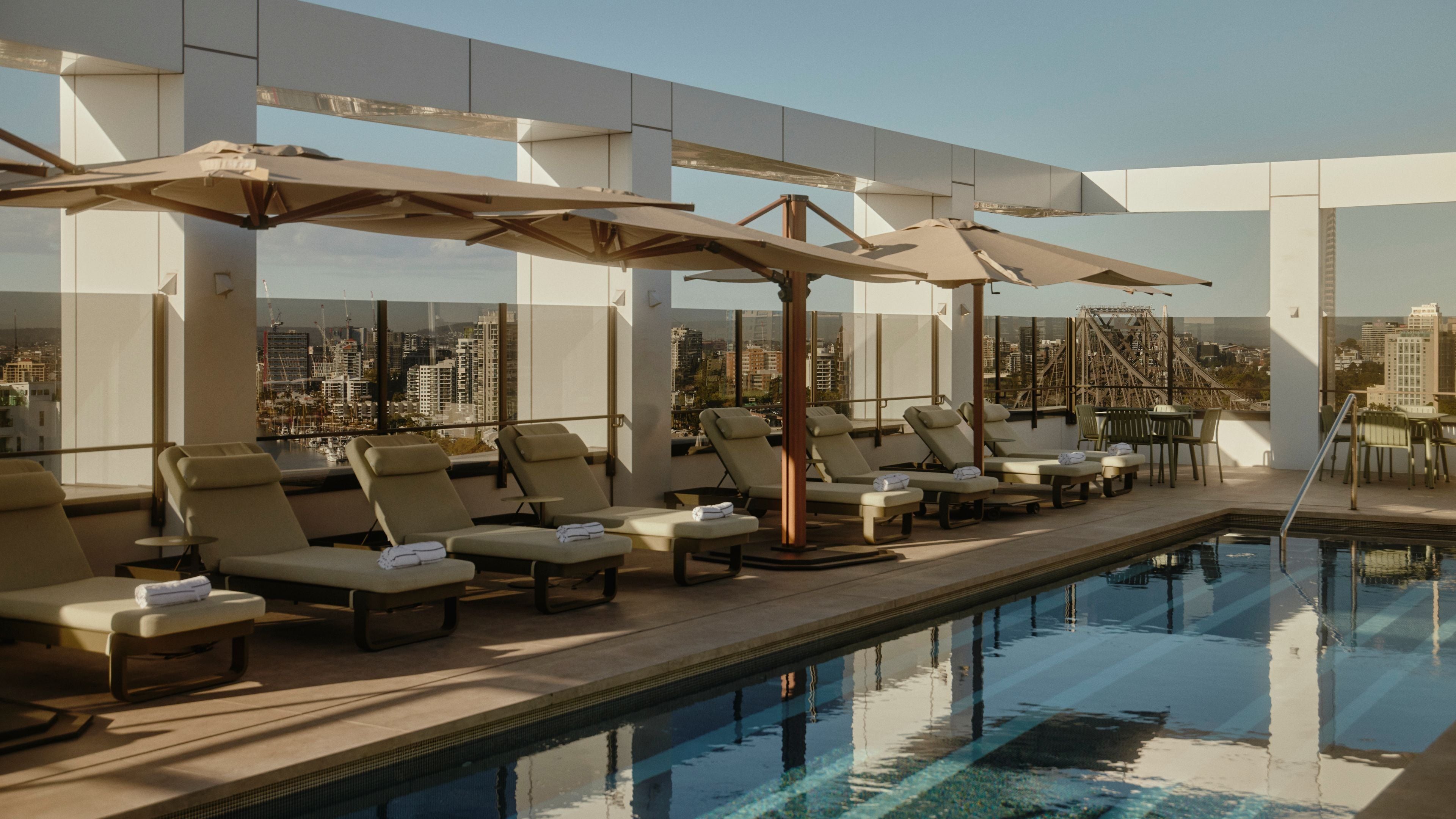 Un espace piscine aménagé sur le toit, avec des chaises longues et des parasols, offrant une vue sur la ville.