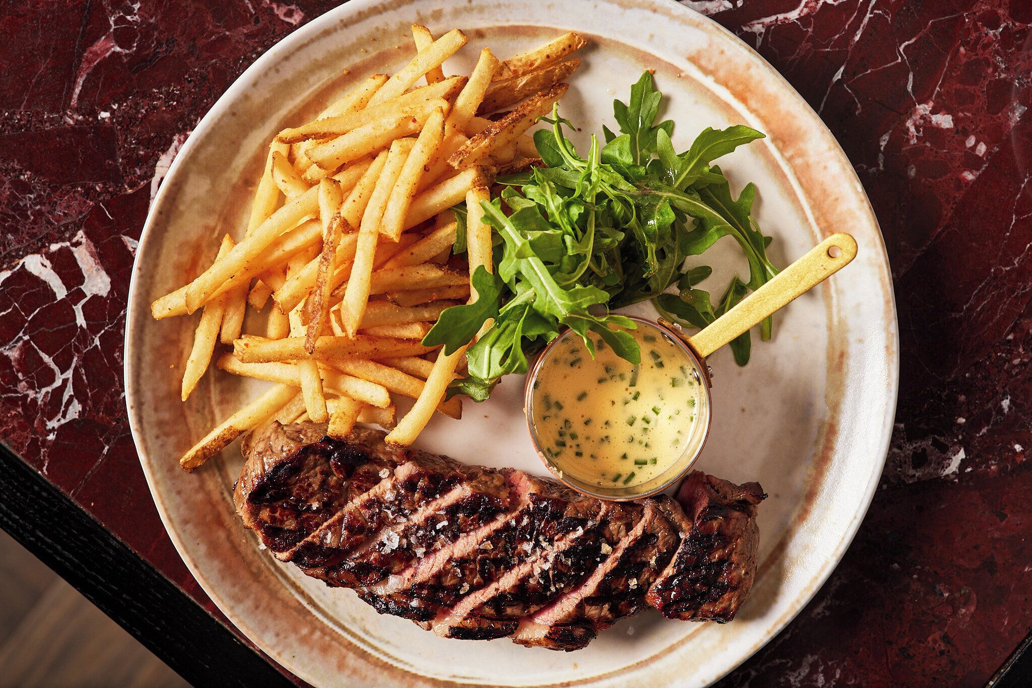 A plate with steak, fries, greens, and a sauce.