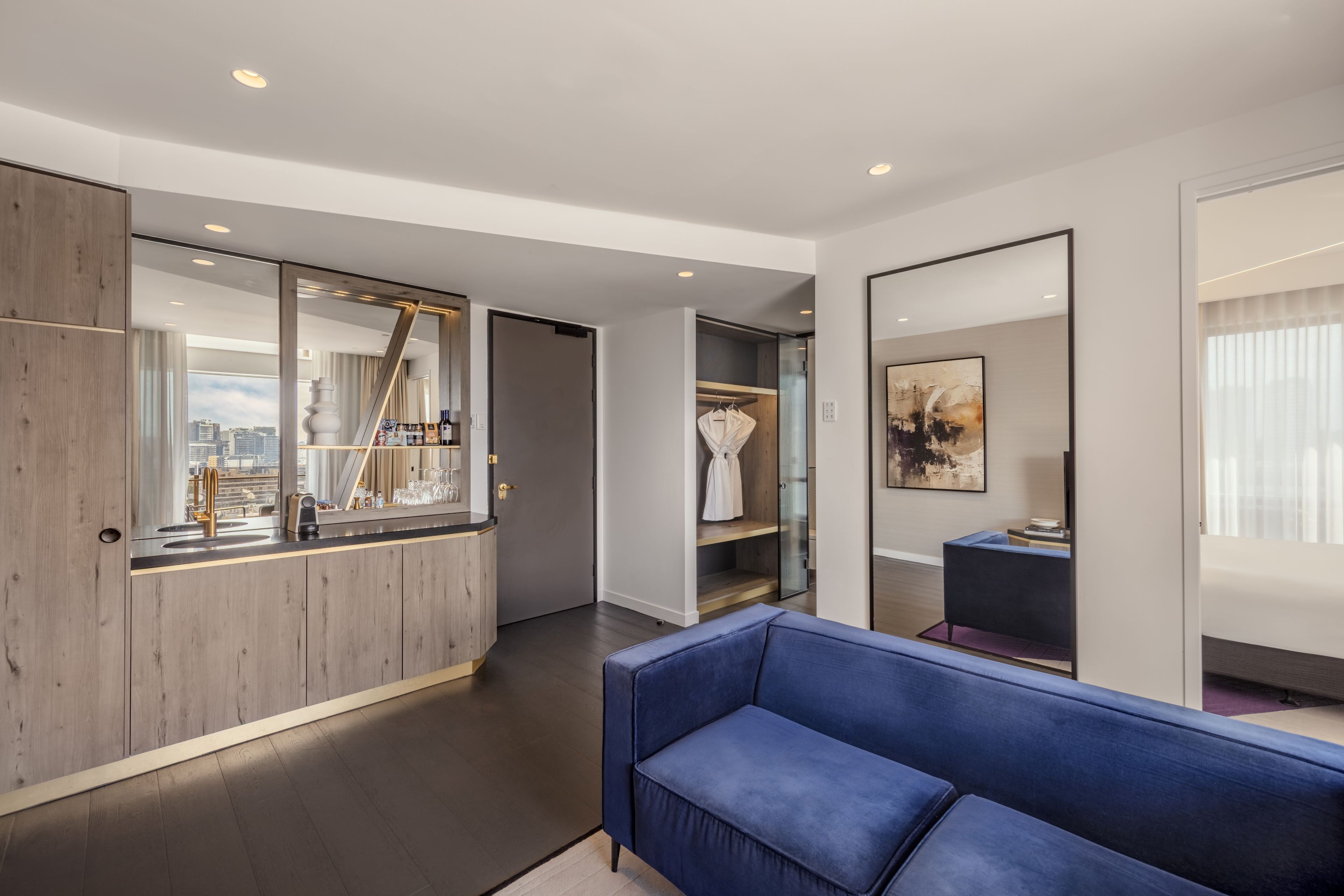 A modern hotel room with a large mirror, a blue sofa, a wardrobe, and a vanity with a mirror.