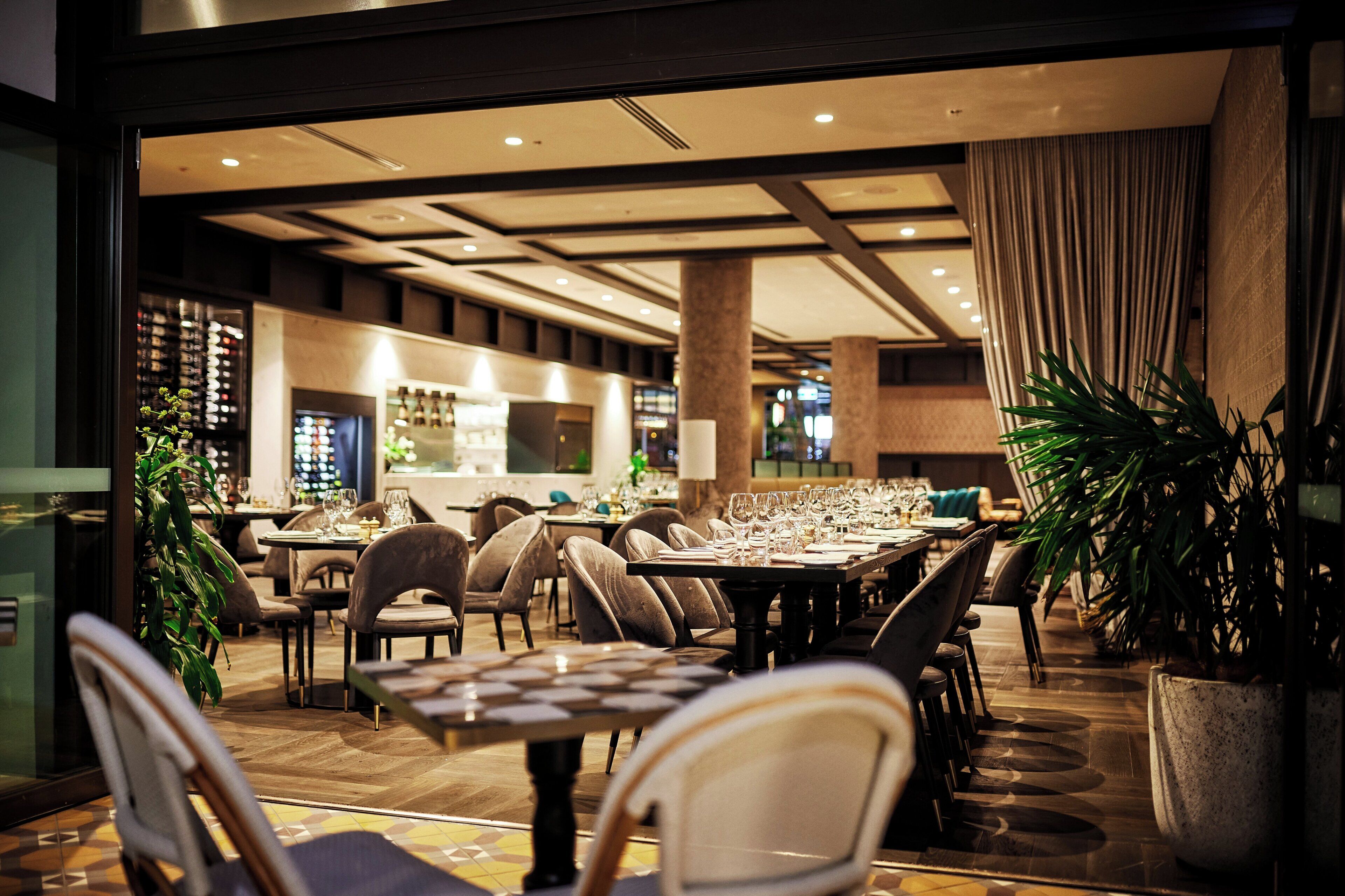 A restaurant with multiple tables and chairs, a bar area, and potted plants.