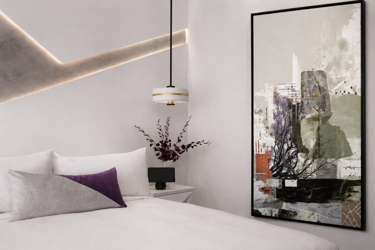 A modern bedroom with a bed, a bedside table with a lamp, and a large abstract painting on the wall.