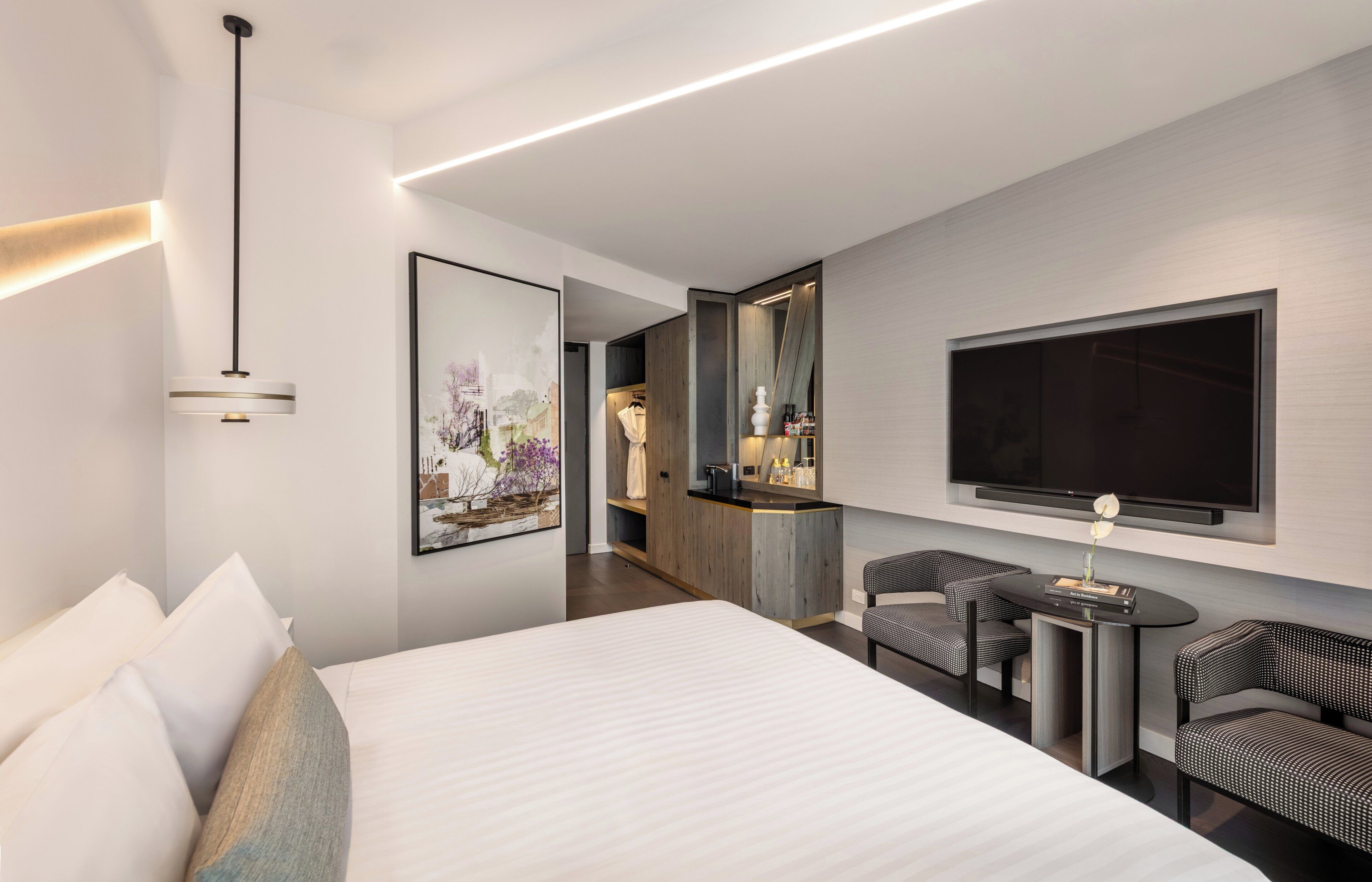 Ein modernes Hotelzimmer mit einem großen Bett, einer Sitzecke mit zwei Sesseln, einem flachbildfernseher an der Wand und einem kleinen Tisch mit einer Vase.