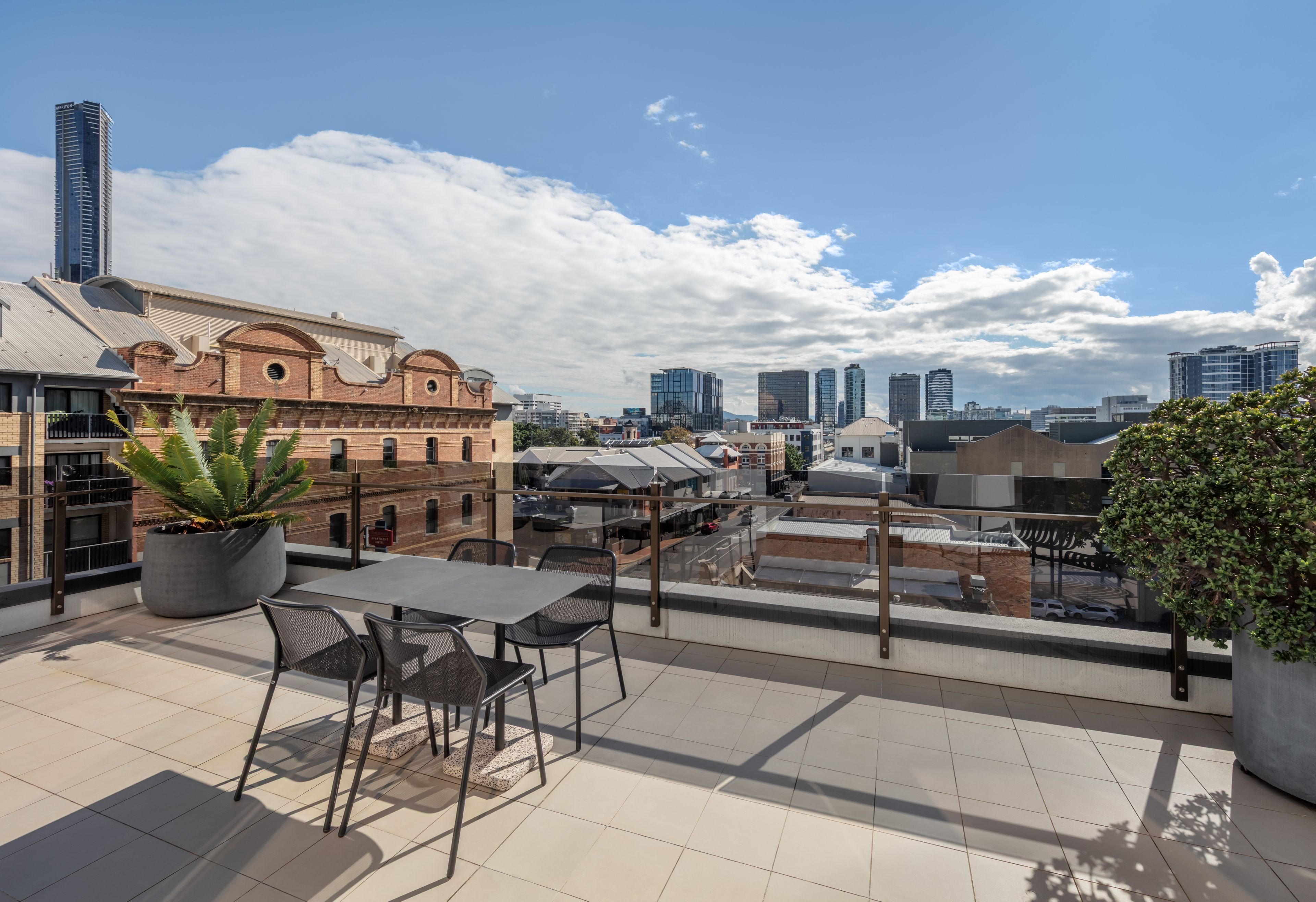 Una terraza en la azotea con mesa y sillas, plantas en macetas y vistas al horizonte de la ciudad.