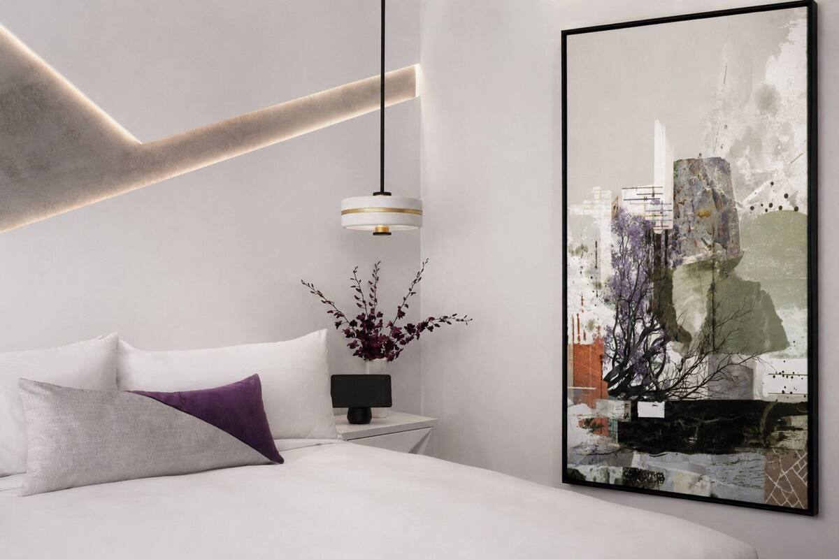 Een moderne slaapkamer met een bed, een nachtkastje met een lamp en een groot abstract schilderij aan de muur.