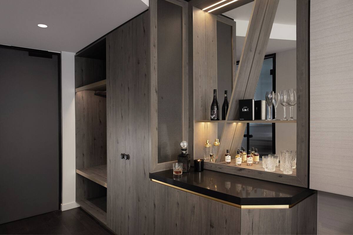 Een moderne bar met houten accenten, een zwart aanrecht en planken met flessen en glazen.
