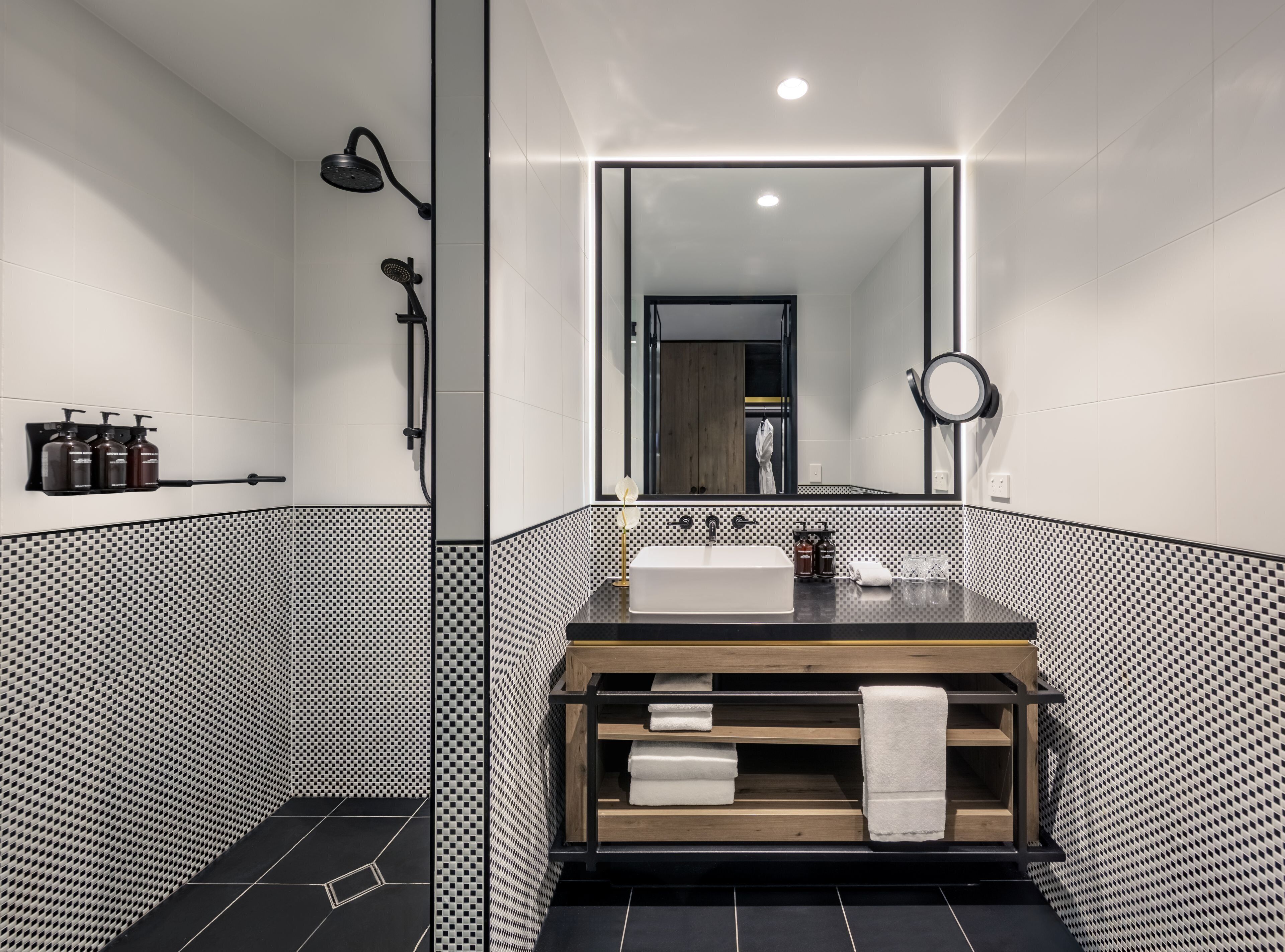 A modern bathroom with a large mirror, a wooden vanity, and a black and white tiled shower area.