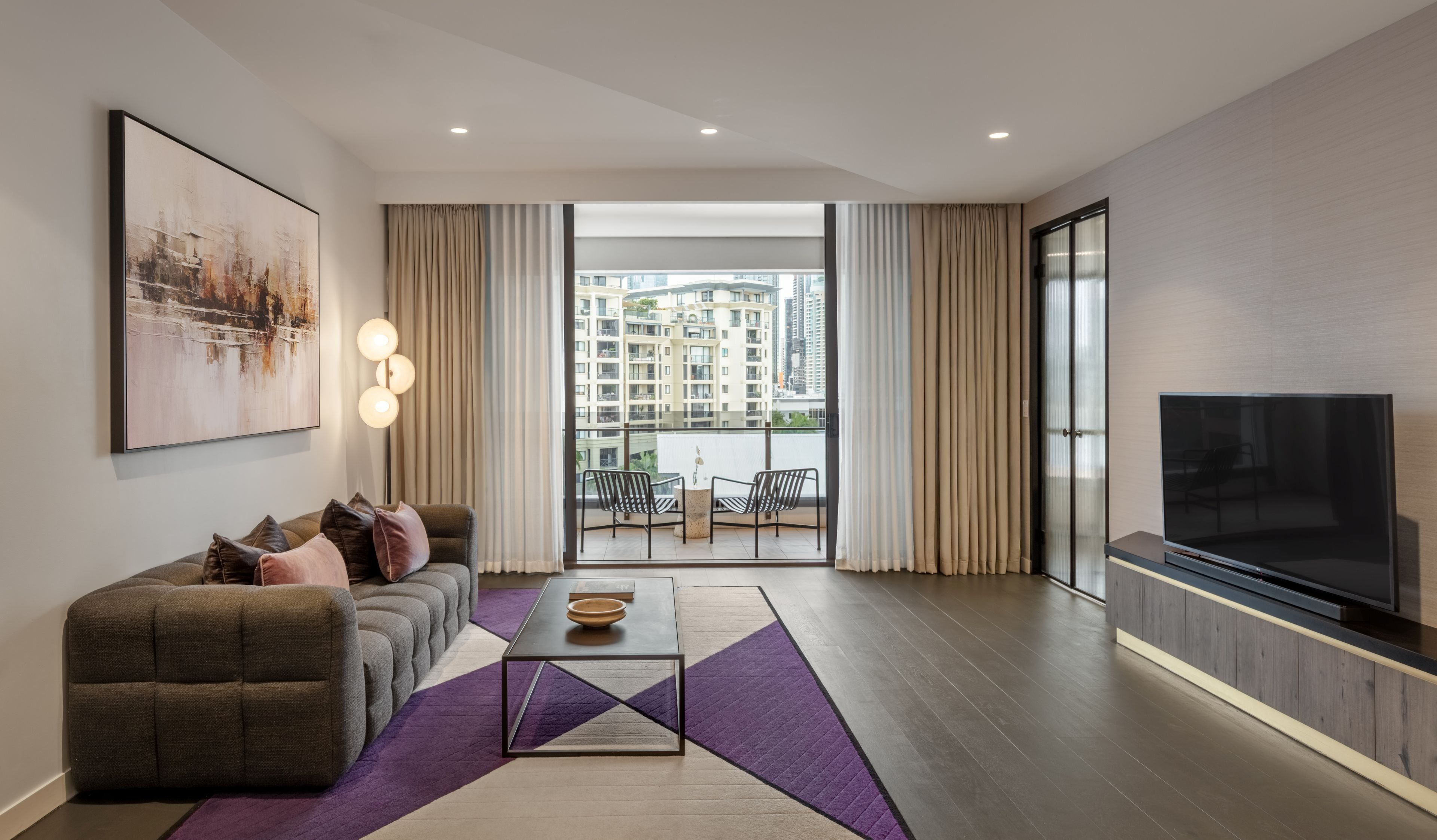 Un salon moderne avec un canapé, une table basse, un téléviseur et un balcon agrémenté de rideaux.