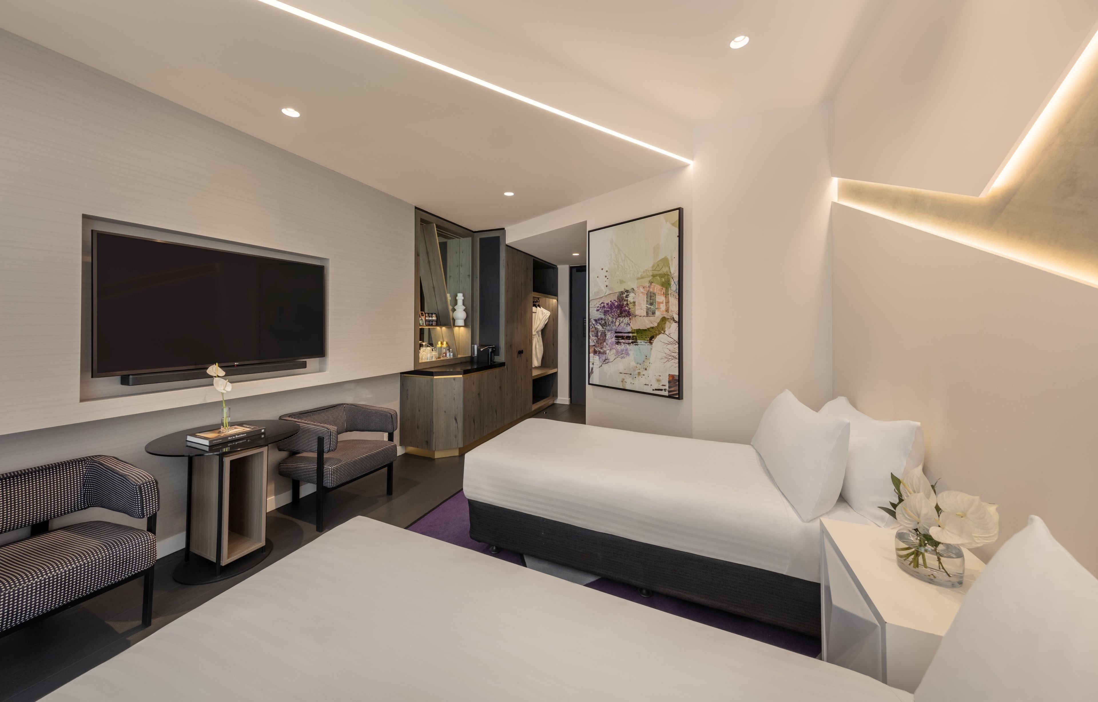 A modern hotel room with a large bed, a flat-screen TV, a seating area with two chairs, a small table, and a large mirror.