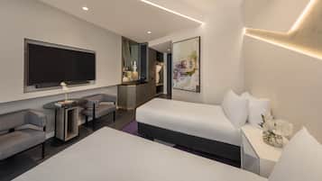 A modern hotel room with a large bed, a flat-screen TV, a seating area with two chairs, a small table, and a large mirror.