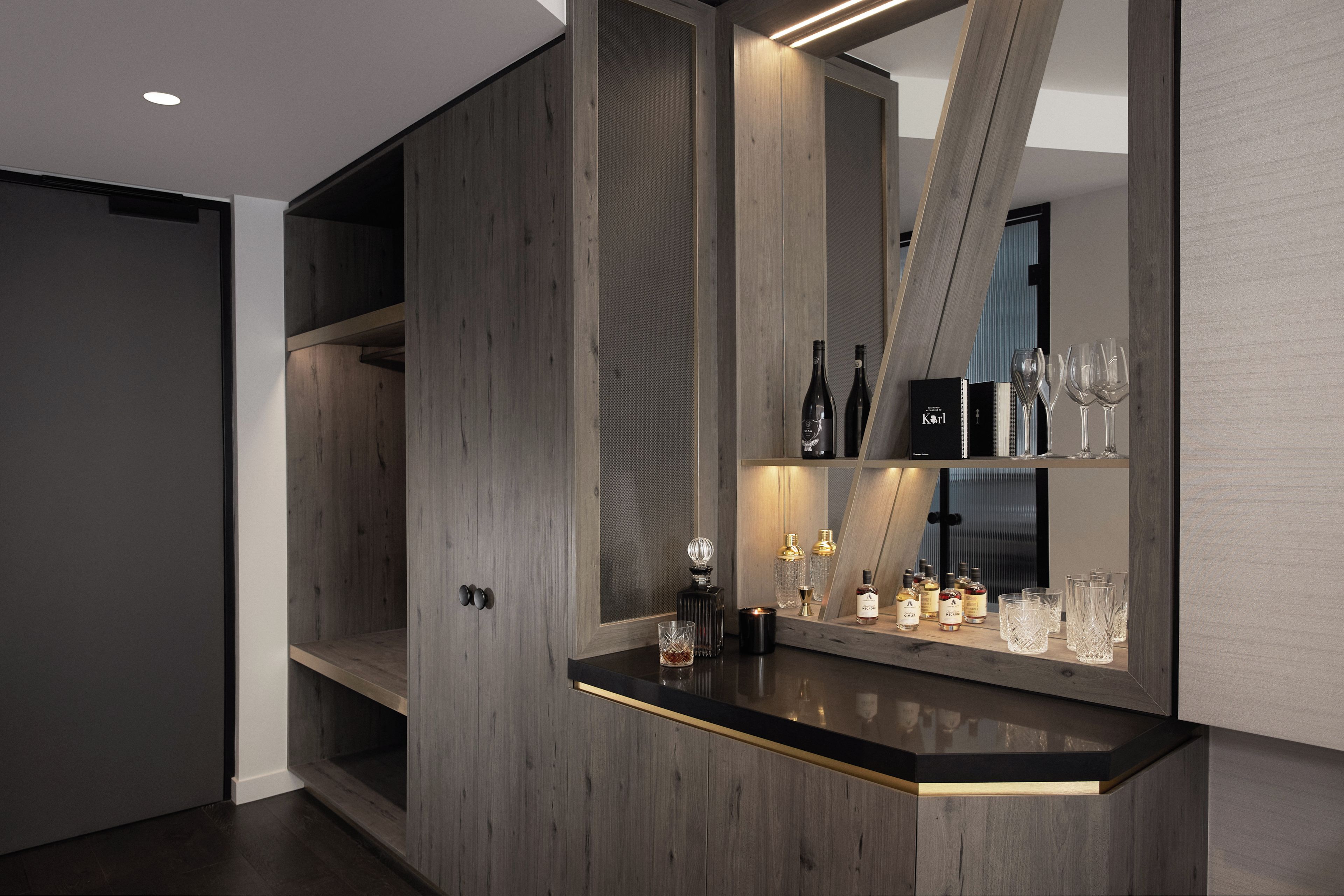 A modern bar area with a wooden finish, a mirrored wall, and a selection of bottles and glasses.