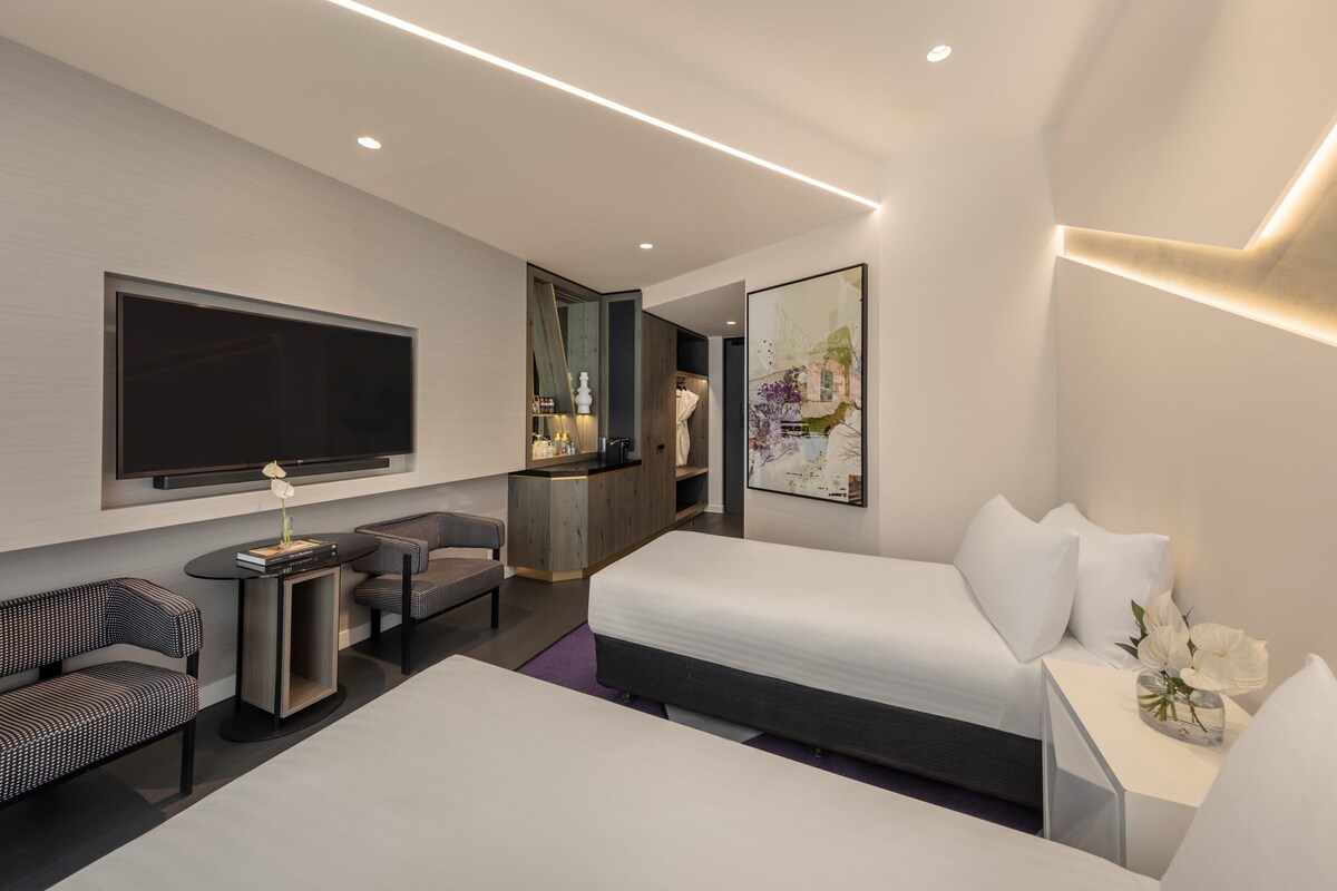 Habitación de hotel moderna con una cama grande, un televisor de pantalla plana, una zona de estar con dos sillones y un escritorio.