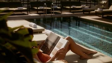 Eine Person entspannt an einem Liegestuhl am Pool und liest ein Buch.