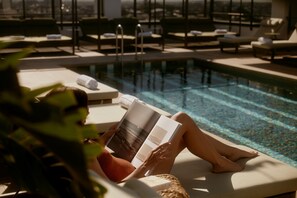 A person relaxing by a poolside lounge chair, reading a book.