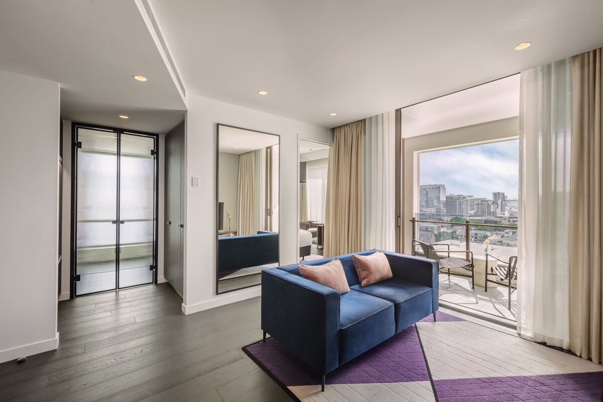 Habitación de hotel moderna con balcón, un espejo grande y un sofá azul.
