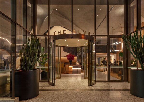 A hotel entrance with a revolving door, glass walls, and potted cacti.