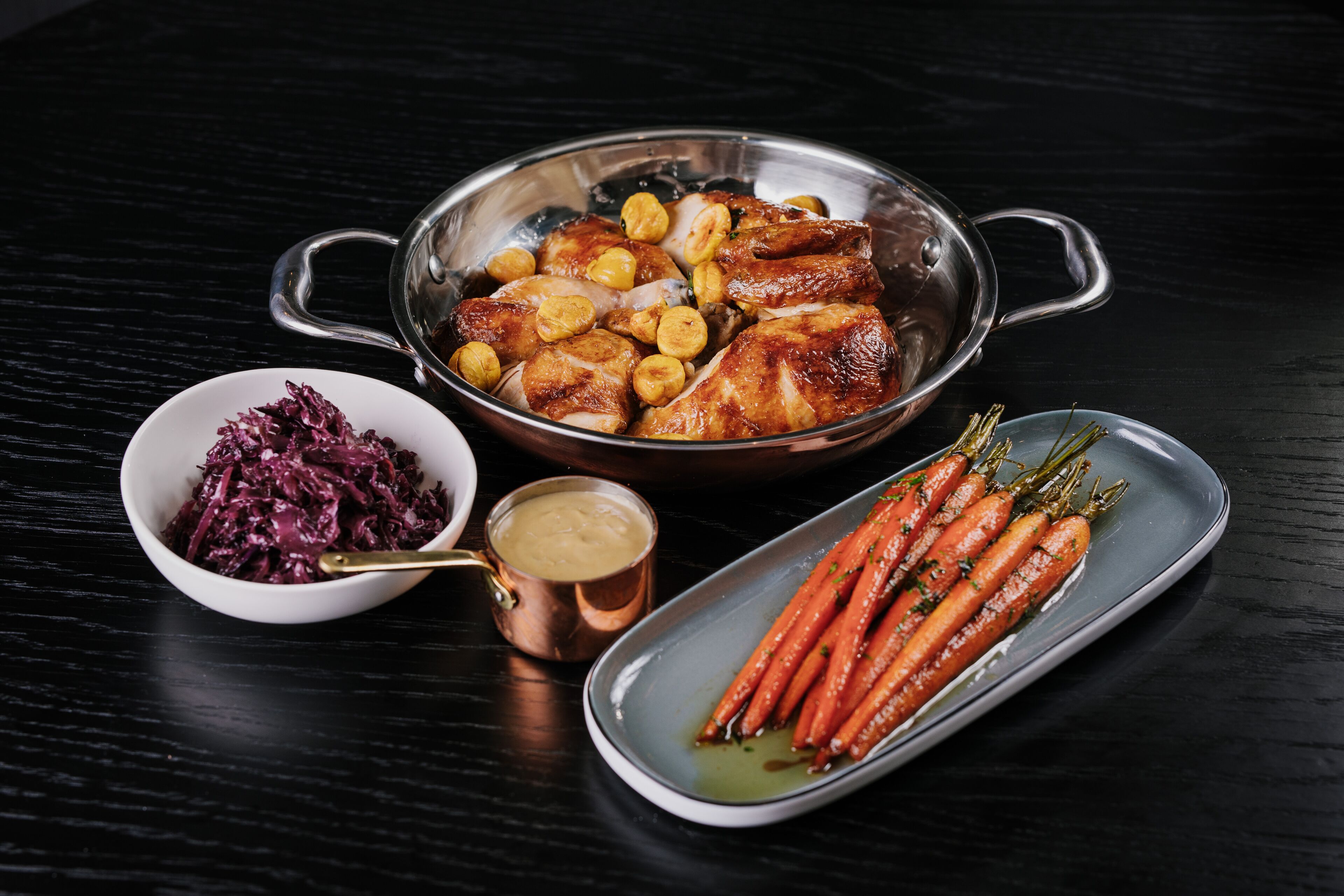 A meal with roasted chicken, carrots, and red cabbage on a dark table.