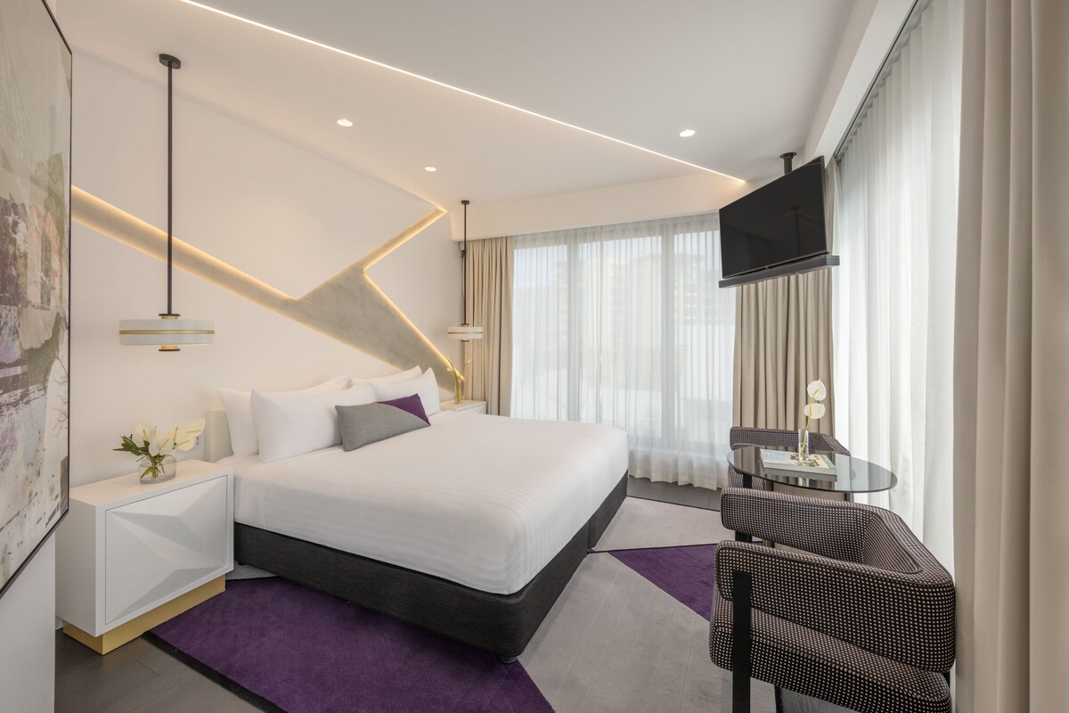 Una habitación de hotel moderna con una cama grande, un escritorio, una silla y un televisor.