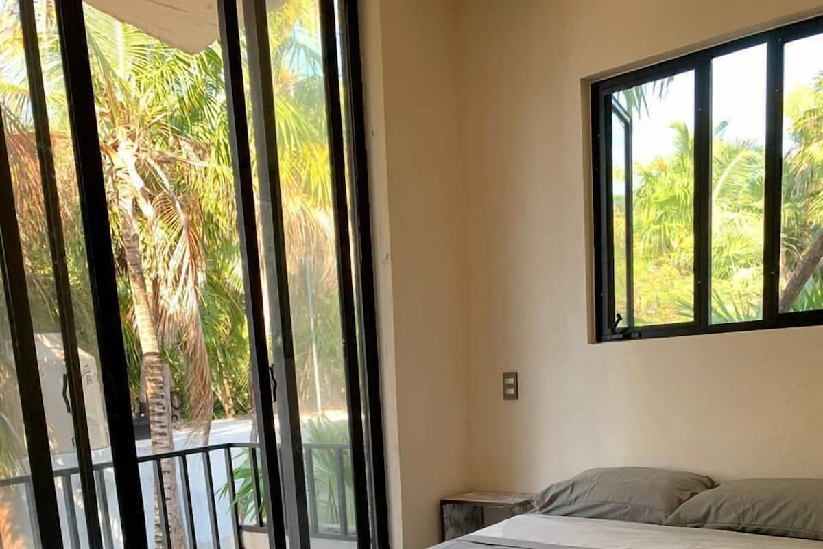 A bedroom with a bed, a window, and a view of palm trees.